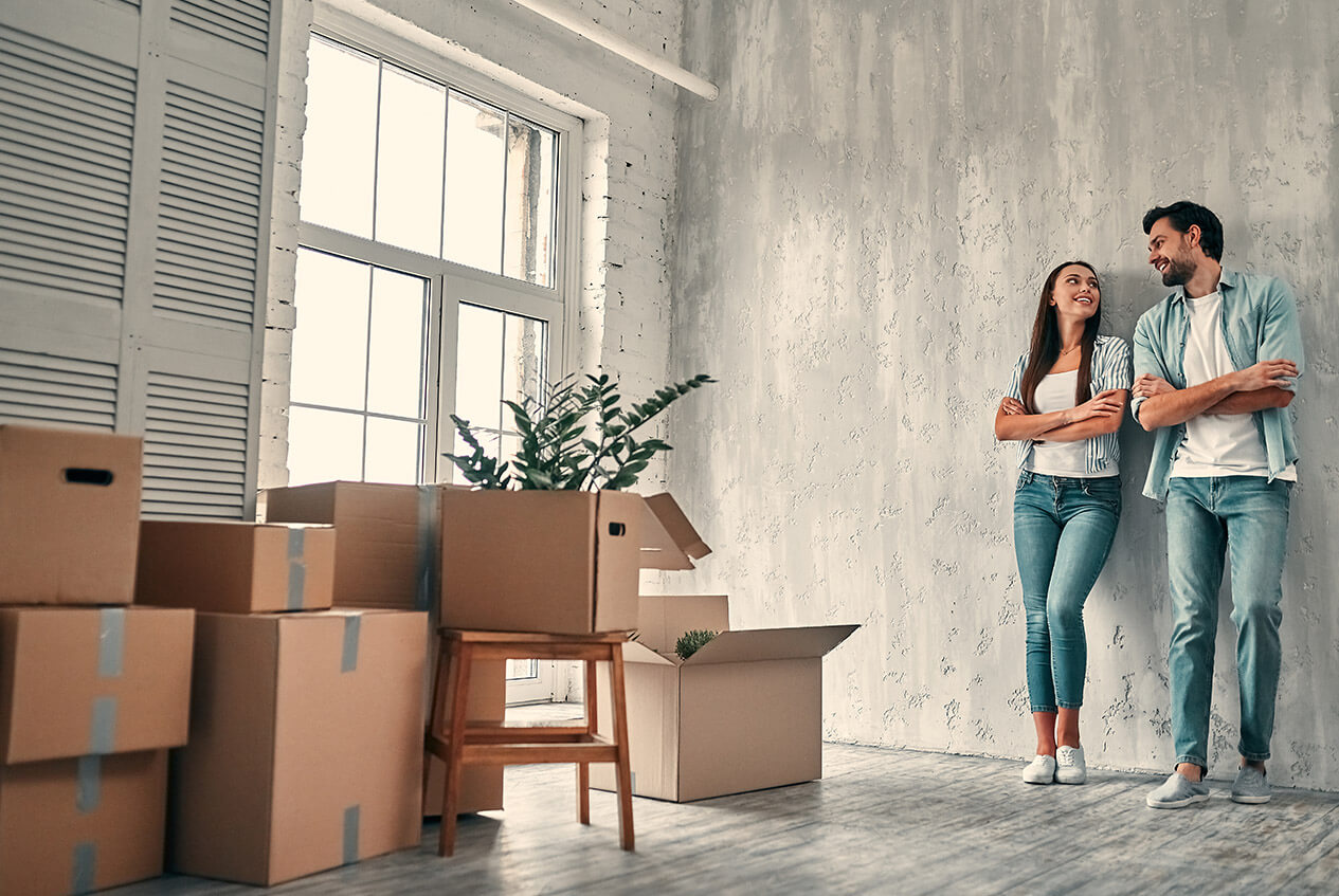 A couple standing beside moving boxes in their new space